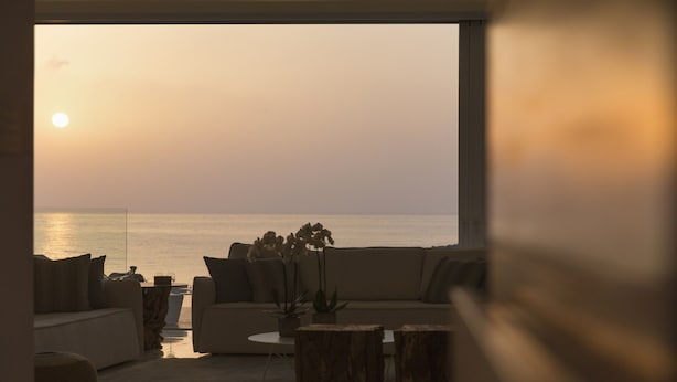 Uma sala de estar com sofá, mesa de centro e vista para o oceano ao pôr do sol.