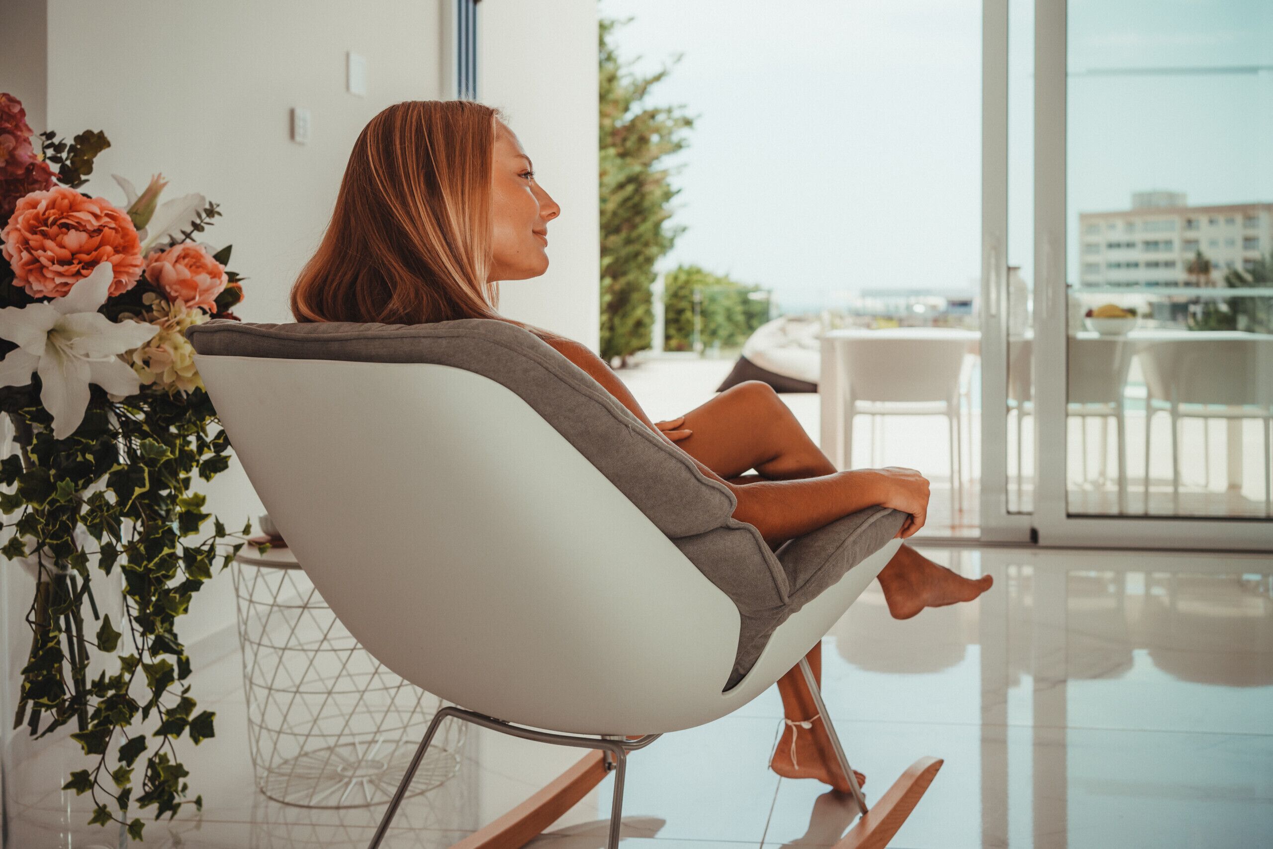 Una persona sentada en una silla moderna con vista a un balcón y paisaje exterior.