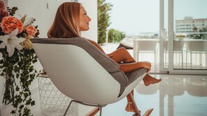 Uma pessoa sentada em uma cadeira moderna com vista para uma varanda e paisagem ao ar livre.