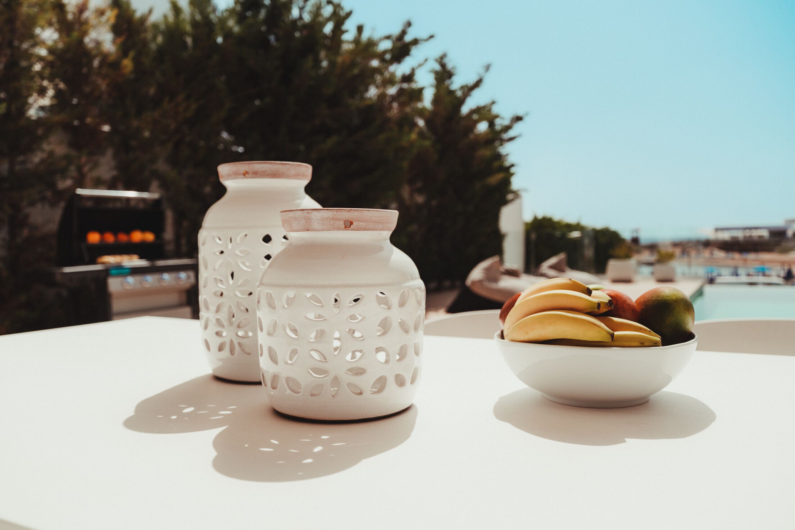 A white table with two white ceramic vases and a bowl of fruit.