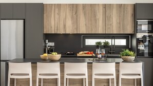Una cocina moderna con armarios oscuros, un revestimiento de pared de madera, una isla central con taburetes de bar y diversos utensilios de cocina.
