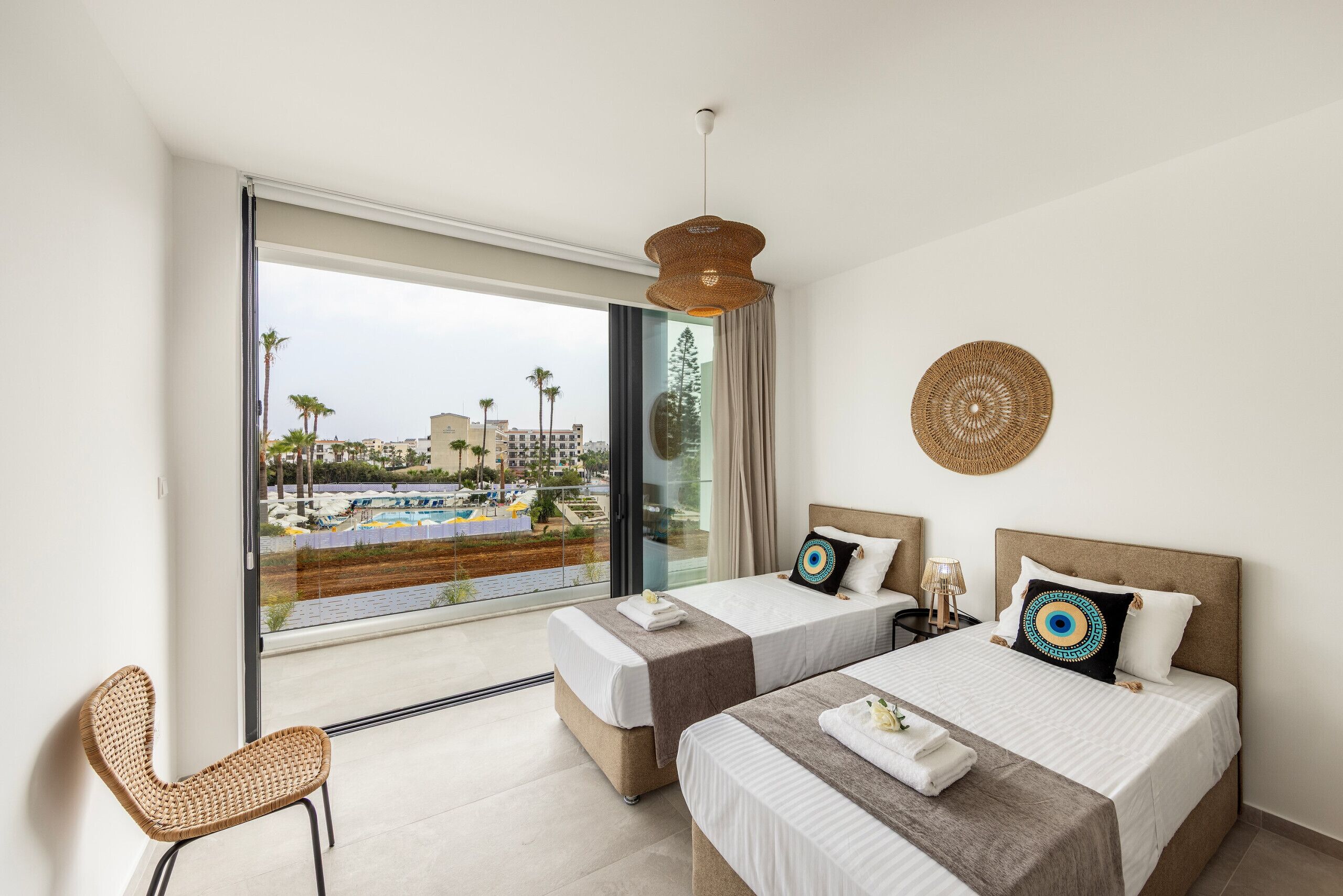 Ein Hotelzimmer mit zwei Betten, einem großen Fenster mit Blick auf einen Pool und Palmen sowie einem gewebten Wandbehang.