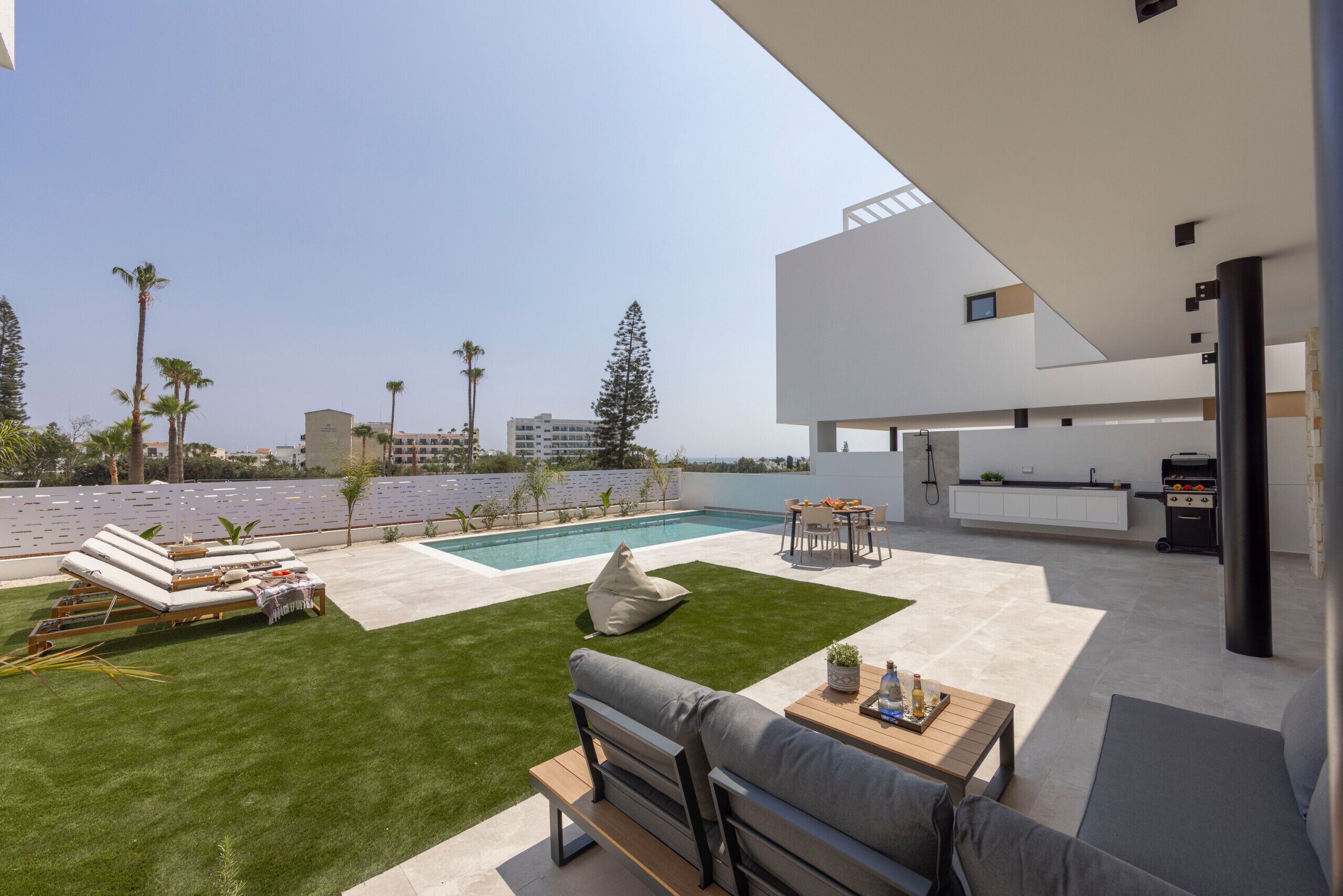 Un espacio exterior moderno con piscina, sillones de descanso, una zona de barbacoa y un área de cocina.