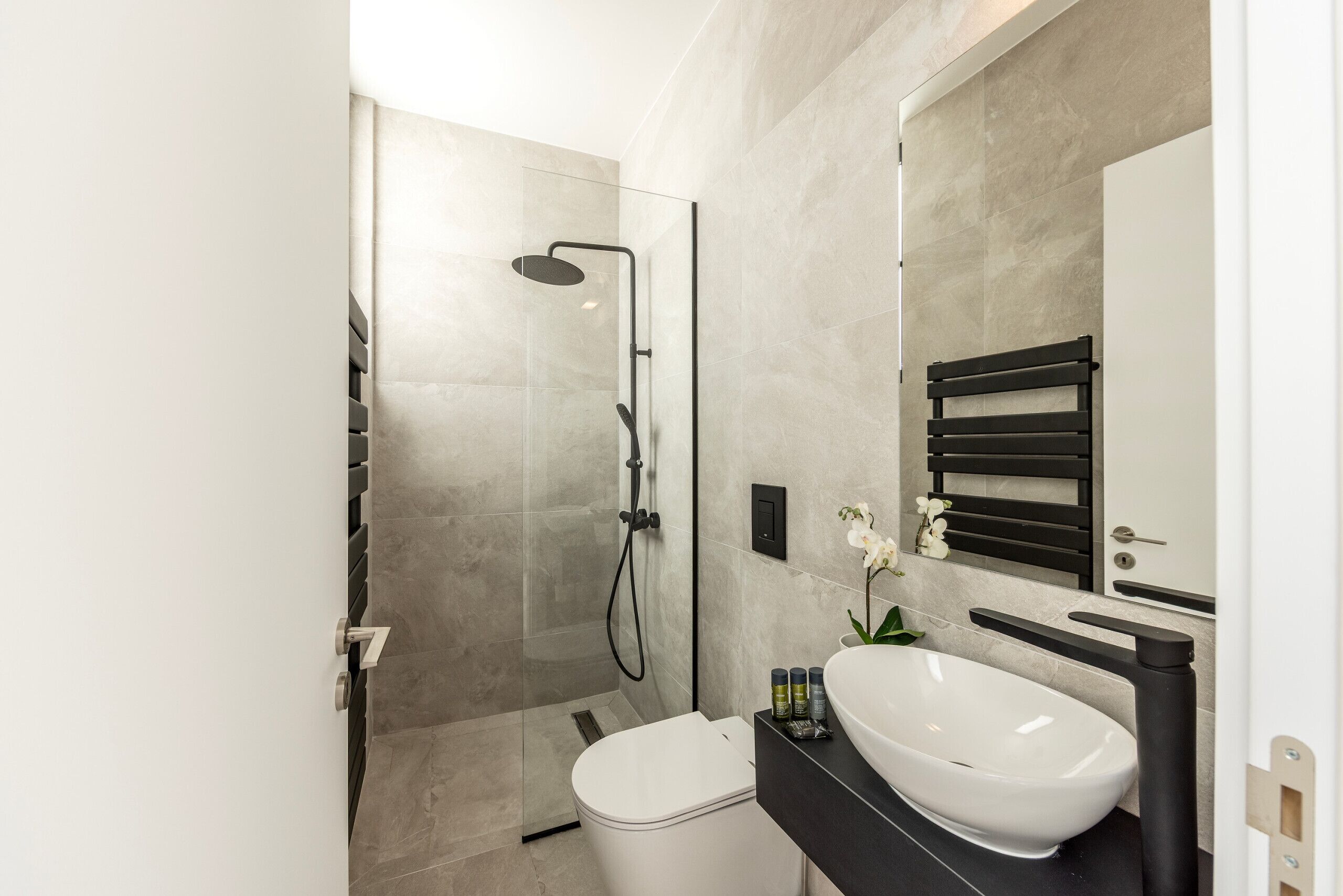 A modern bathroom with a glass-enclosed shower, a white toilet, and a black vanity with a white sink.