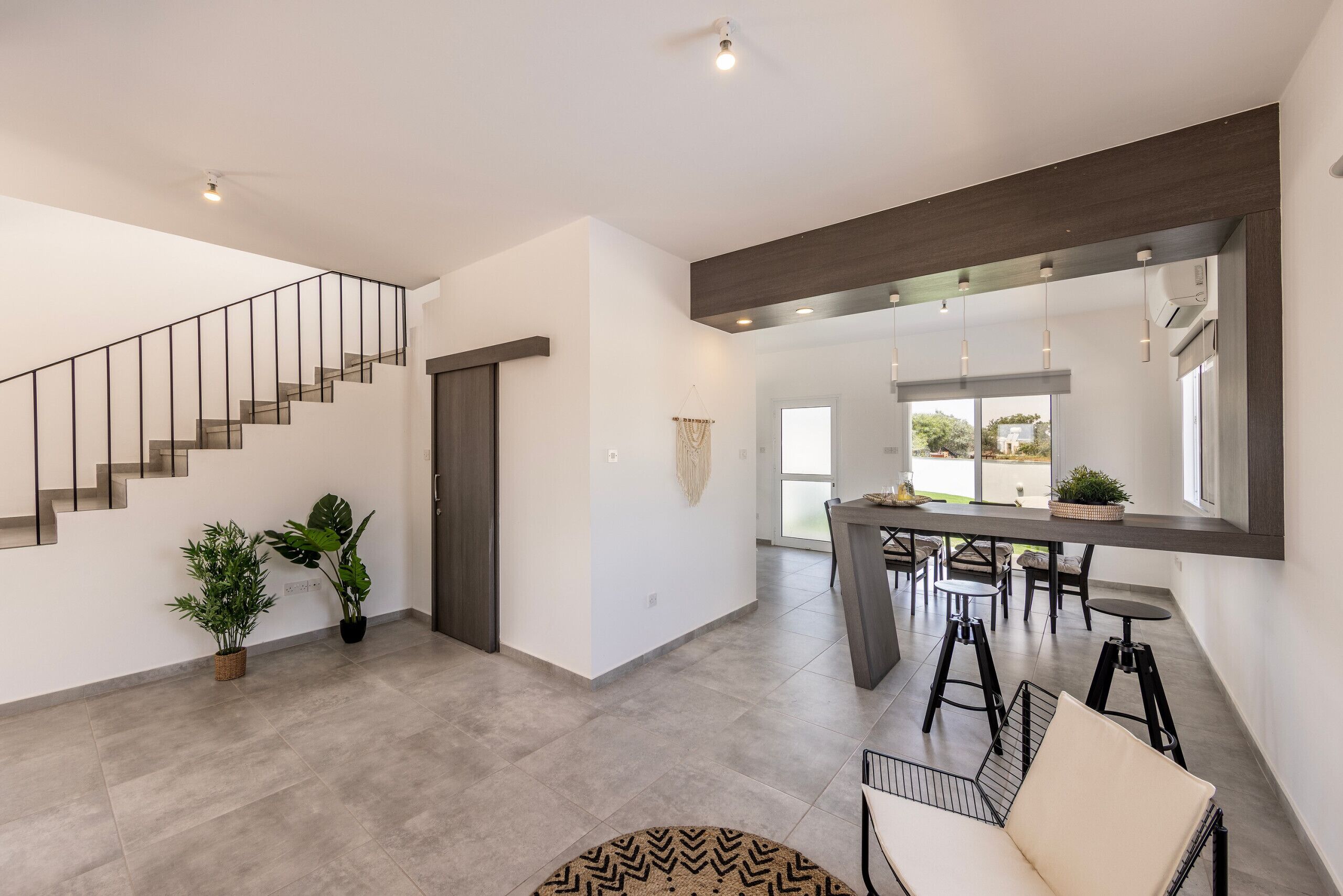 Un interior moderno con una escalera, un comedor y una zona de estar con sofá y sillones.