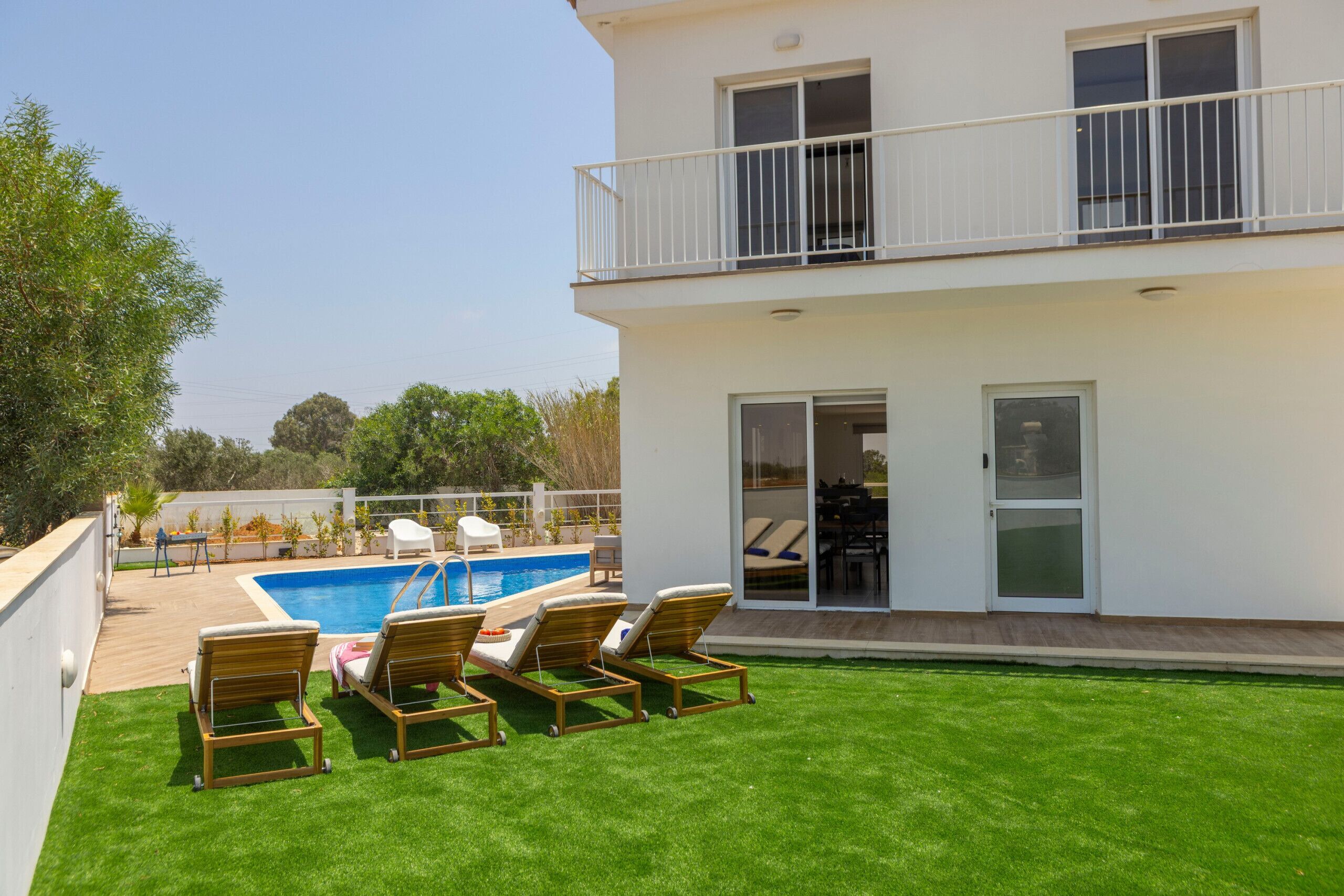 Una casa de dos pisos con piscina, balcón y césped cuidado.