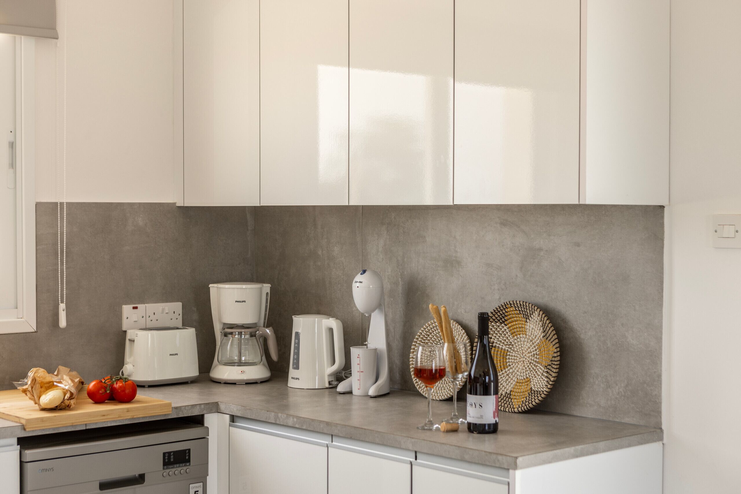 Una cocina moderna con armarios blancos, una cafetera, un tostador y una botella de vino sobre la encimera.