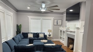 Ein Wohnzimmer mit Ecksofa, Kamin, Deckenventilator und Flachbildfernseher.
