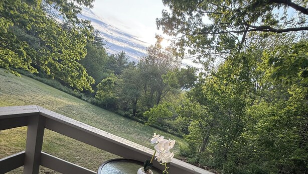 Un patio con una mesa redonda de vidrio y dos sillas, con vistas a un área verde con árboles.
