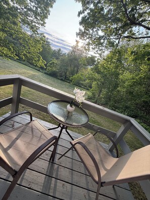 A patio with a round glass table and two chairs, overlooking a grassy area with trees.