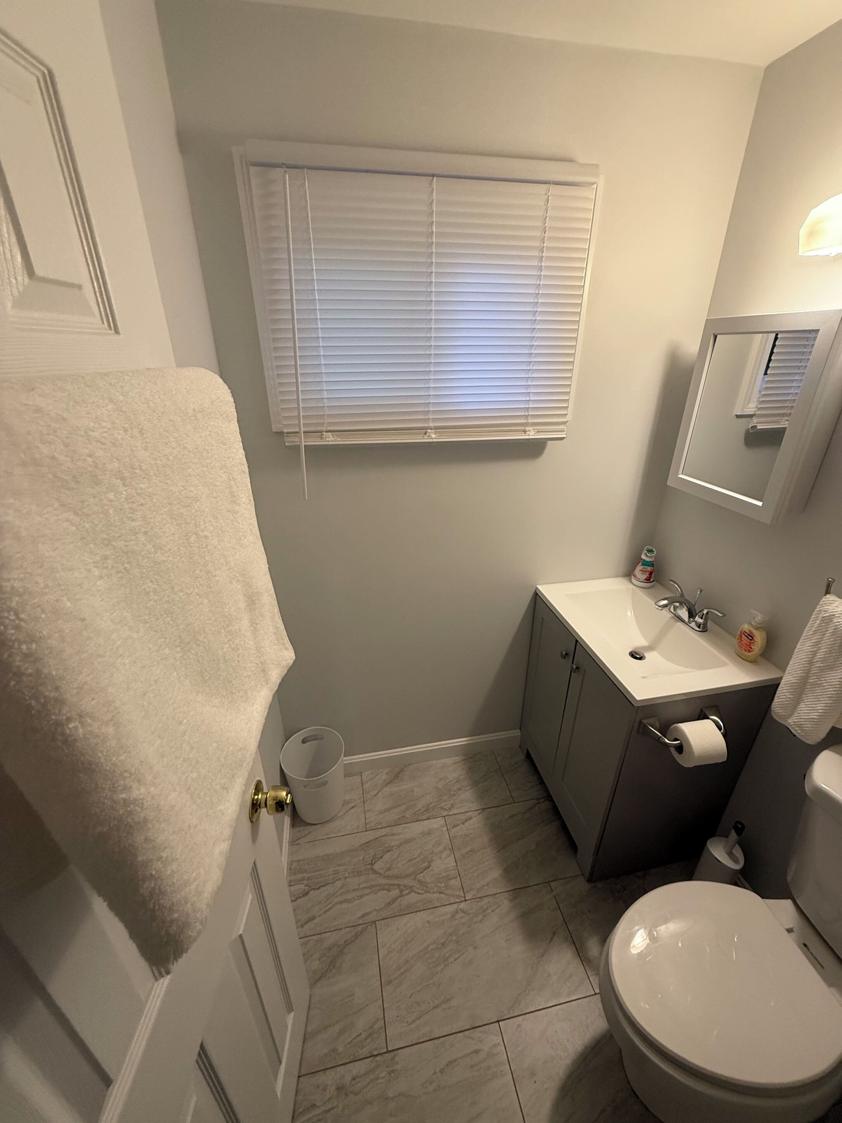 A bathroom with a toilet, sink, and window with blinds.