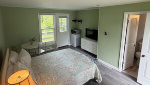 Un dormitorio con cama, lámpara de noche, cómoda, televisor y una pequeña mesa con sillas.
