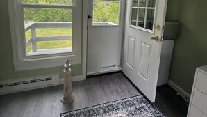 Una habitación con un ventanal grande, una puerta, un radiador, una alfombra y una pequeña estatua.
