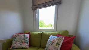 A green sofa with floral and red cushions in a room with a window and a view of greenery outside. - Shell on the Rhön beach with whirlpool (Wartmannsroth)