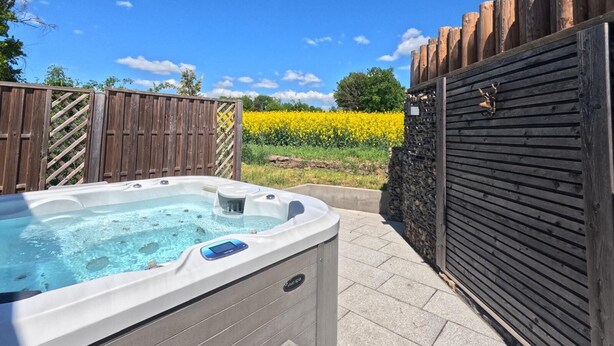 A hot tub with a digital control panel, surrounded by a wooden fence and a stone wall, with a field of yellow flowers in the background. - Shell on the Rhön beach with whirlpool (Wartmannsroth)