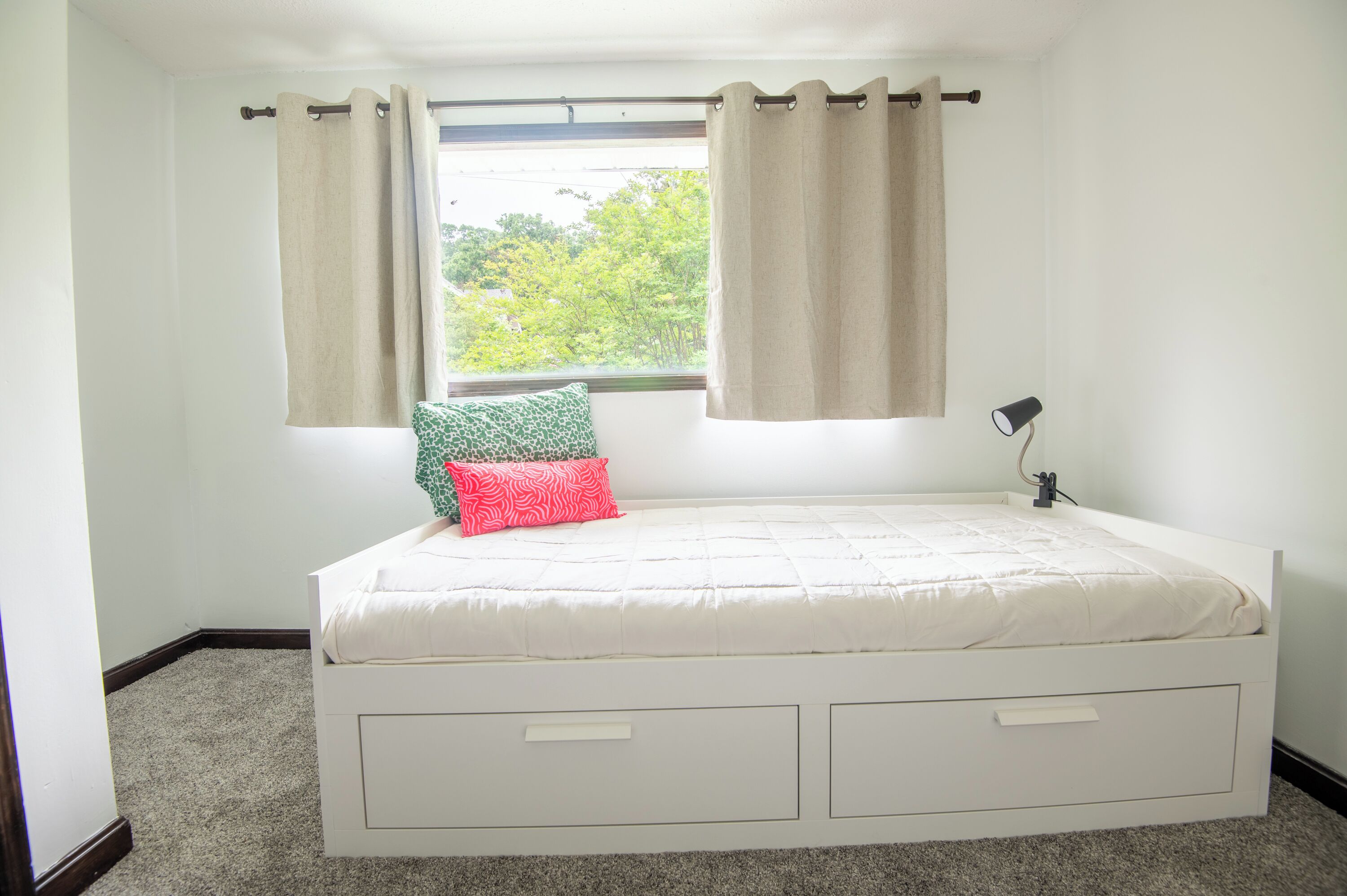 Un dormitorio con cama, dos almohadas, una lámpara y una ventana con cortinas.