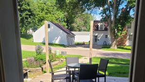 Una terraza de madera con mobiliario exterior, vista a una calle residencial y un espacio con césped.