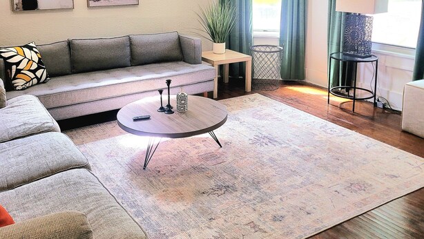 Una sala de estar con un sofá, una mesa de centro, una lámpara y un ventanal con cortinas.