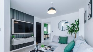 A modern living room with a flat-screen TV, a sofa, a coffee table, and a potted plant.