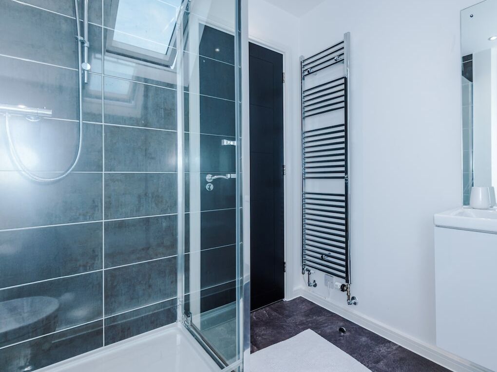 Un baño moderno con cabina de ducha de vidrio, toallero en la pared y lavamanos blanco con espejo.