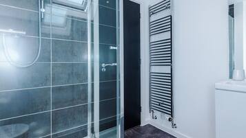 Un baño moderno con cabina de ducha de vidrio, toallero en la pared y lavamanos blanco con espejo.