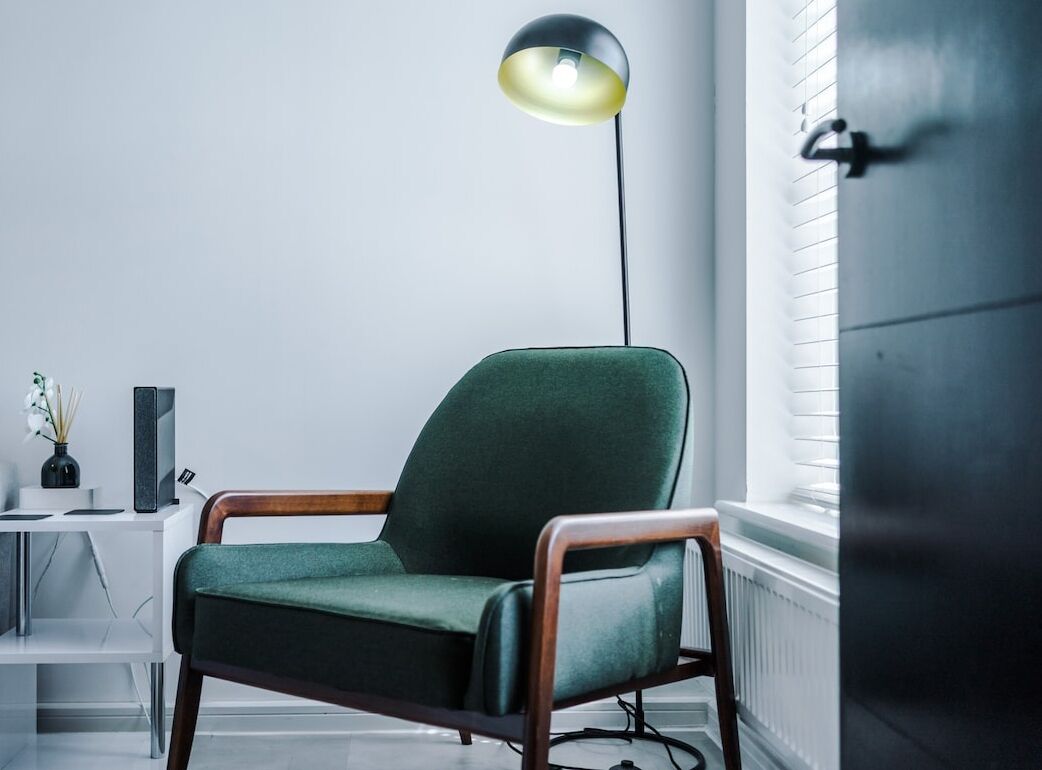 A modern room with a green armchair, a floor lamp, a white console table, and a radiator.