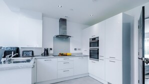 A modern kitchen with white cabinets, a stainless steel range hood, an oven, and a coffee maker.