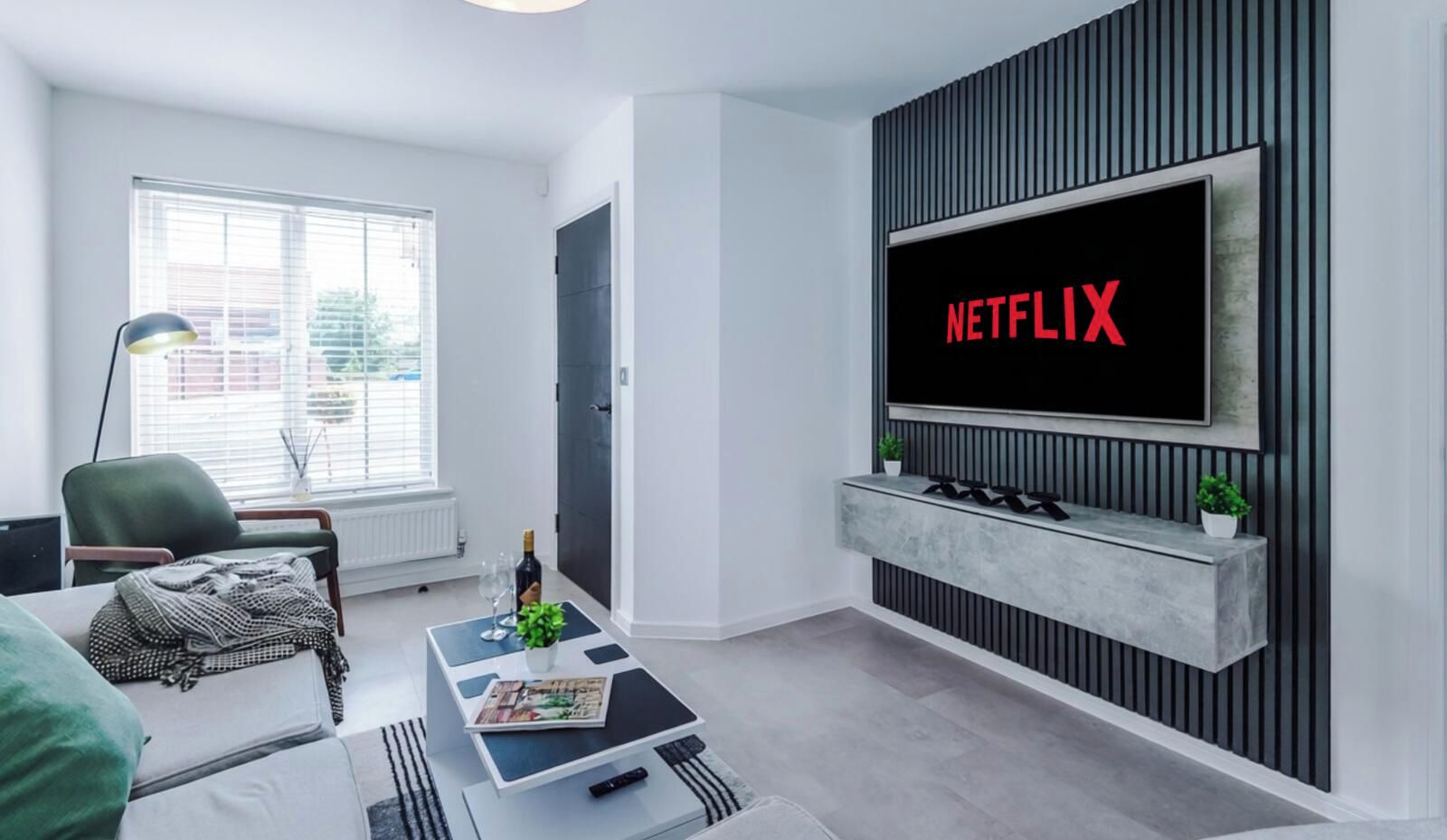 A modern living room with a flat-screen TV mounted on a wall, a sofa, a coffee table with a magazine, and a lamp.