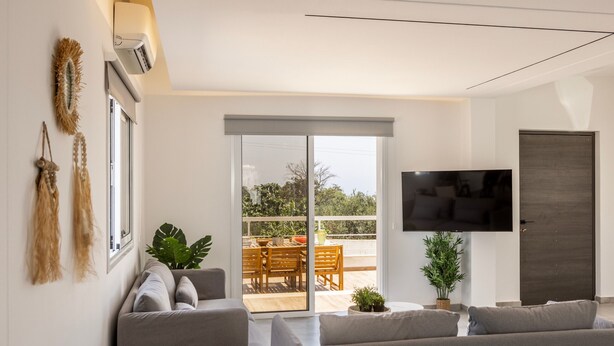 Een moderne woonkamer met een bank, een flatscreen-tv en een schuifdeur naar een terras.