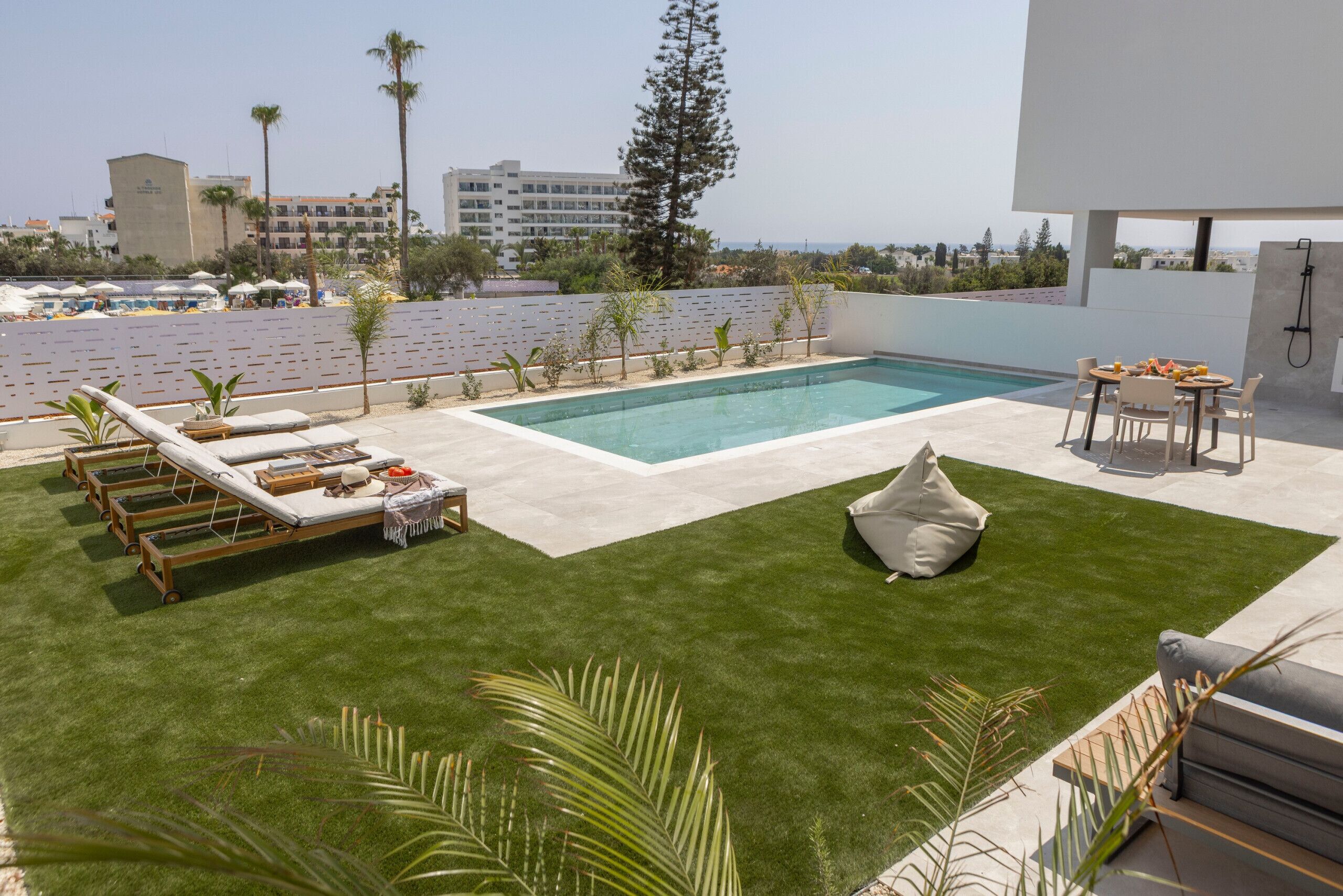 A modern outdoor pool area with lounge chairs, a small seating area, and a view of the cityscape.
