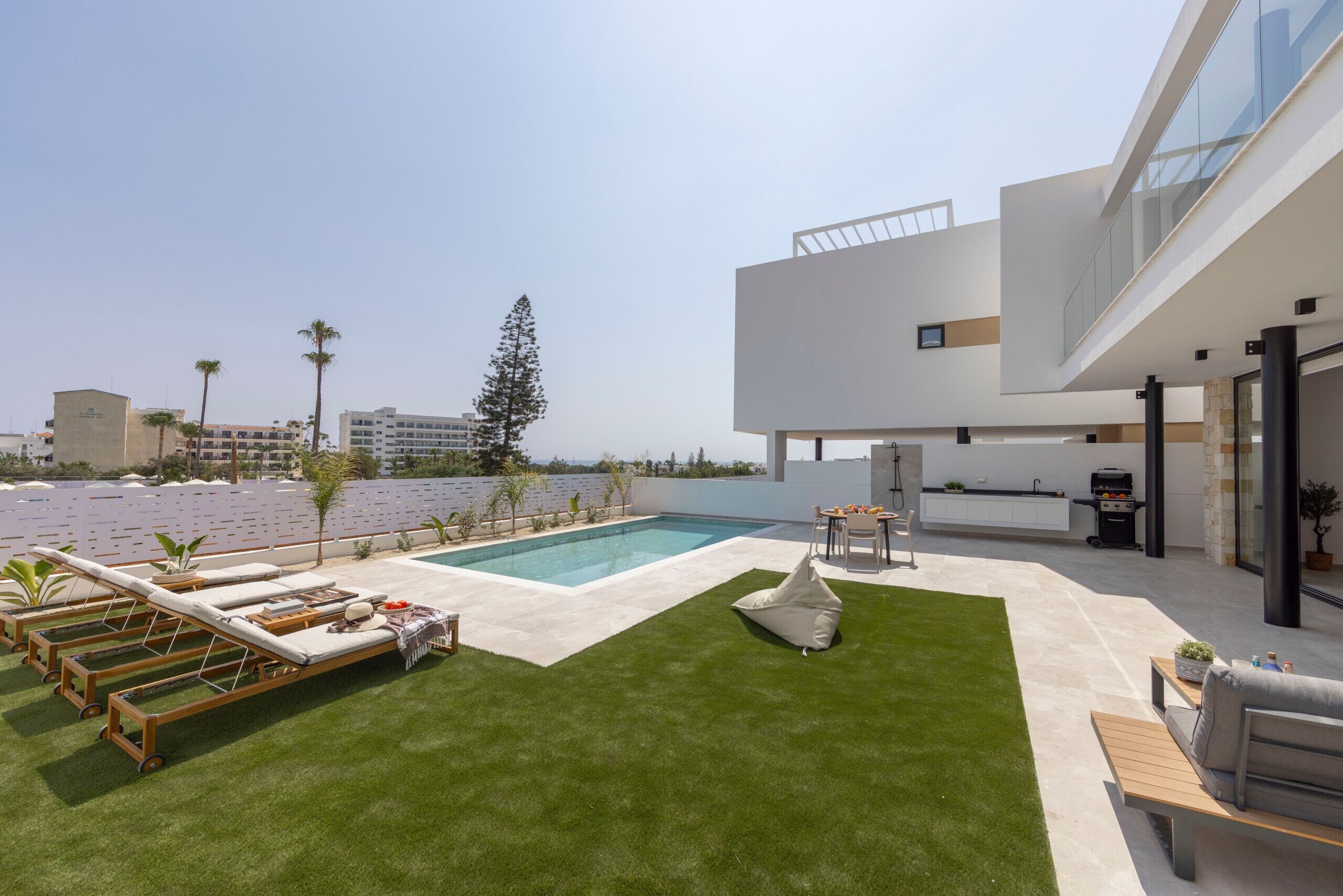 A modern outdoor pool area with lounge chairs, a barbecue, and a view of the ocean.