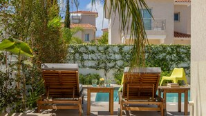A poolside area with two wooden lounge chairs, a small table with drinks, and a yellow chair.