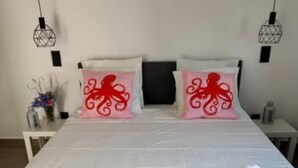 Un lit bien fait, avec des draps blancs, deux coussins décoratifs ornés de motifs de poulpes rouges et deux serviettes enroulées posées sur le lit.