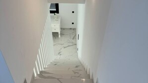 Un escalier moderne avec un sol en marbre mène à une pièce où se trouvent une commode blanche et une petite table.