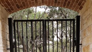 A gated entrance with a brick archway, a metal gate with star-shaped decorations, and a bench outside.