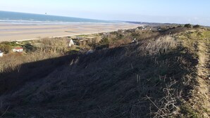 A coastal landscape with a beach, houses, and a hill.