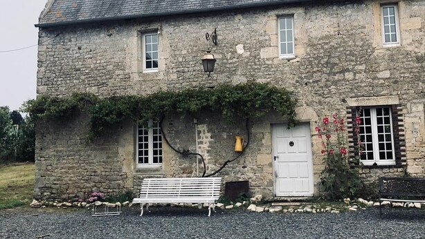 A stone building with a sloped roof, a white door, and a bench in front.