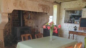 A rustic dining area with a brick fireplace, wooden chairs, and a table set with a green tablecloth.