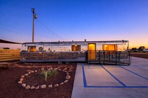 A stationary RV with a metal exterior, a small porch area, and a paved driveway. - Premium Airstream with Private Hot Tub (Unit I) - 3 Person Premium Airstream (Williams)