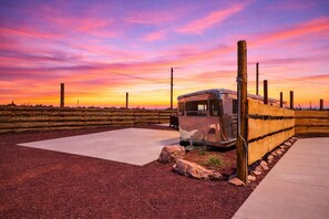 Una caravana vintage estacionada en un área ajardinada con un patio de hormigón y una valla de madera.