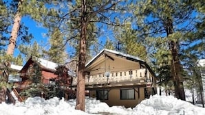 A two-story lodge with a balcony, surrounded by tall pine trees and snow-covered ground.