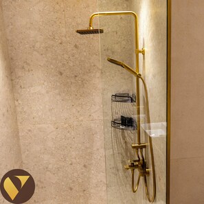 A modern shower with a gold finish, a handheld showerhead, and a wall-mounted control panel.