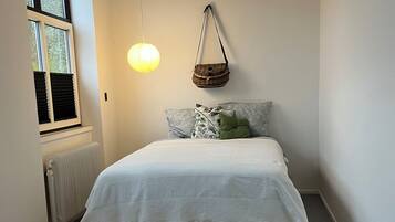 A bedroom with a bed, a hanging basket, a radiator, and a window.