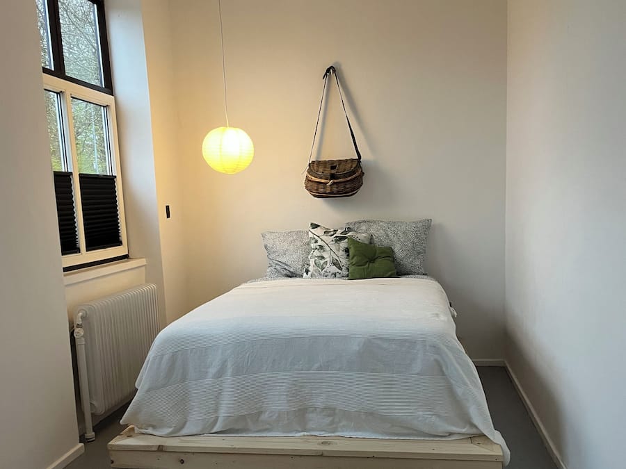 Un dormitorio con cama, una cesta colgante, un radiador y una ventana.