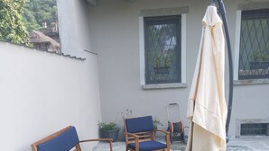 A patio area with wooden chairs and a table, a covered umbrella, and a hose. - The Ladybirds Residence (Piemonte)