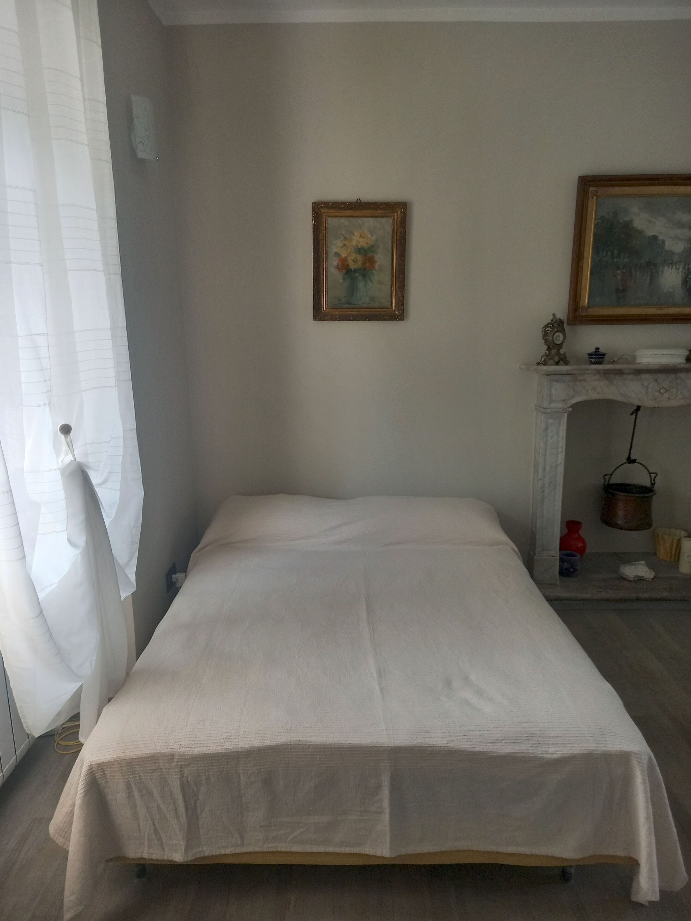 Une chambre à coucher avec un lit, un tableau, une cheminée et une fenêtre avec des rideaux.