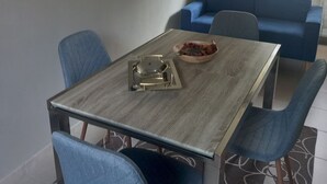 A dining area with a wooden table and blue chairs, a blue sofa, a stone wall, and a painting of flowers on the wall. - The Ladybirds Residence (Piemonte)