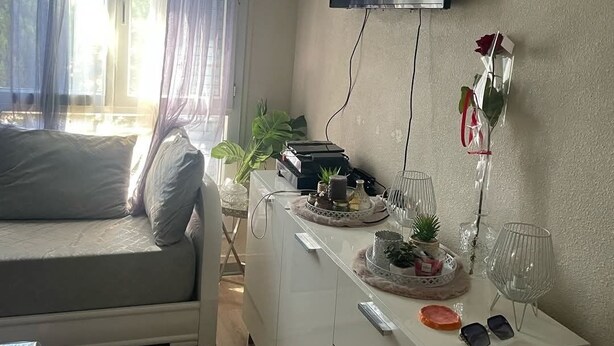 A modern room with a sofa, a TV mounted on the wall, a small cabinet with decorative items, and a window with curtains. - Festival apartment (Avignon)
