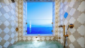 Una bañera con vista al océano a través de una ventana, un cabezal de ducha y un grifo.