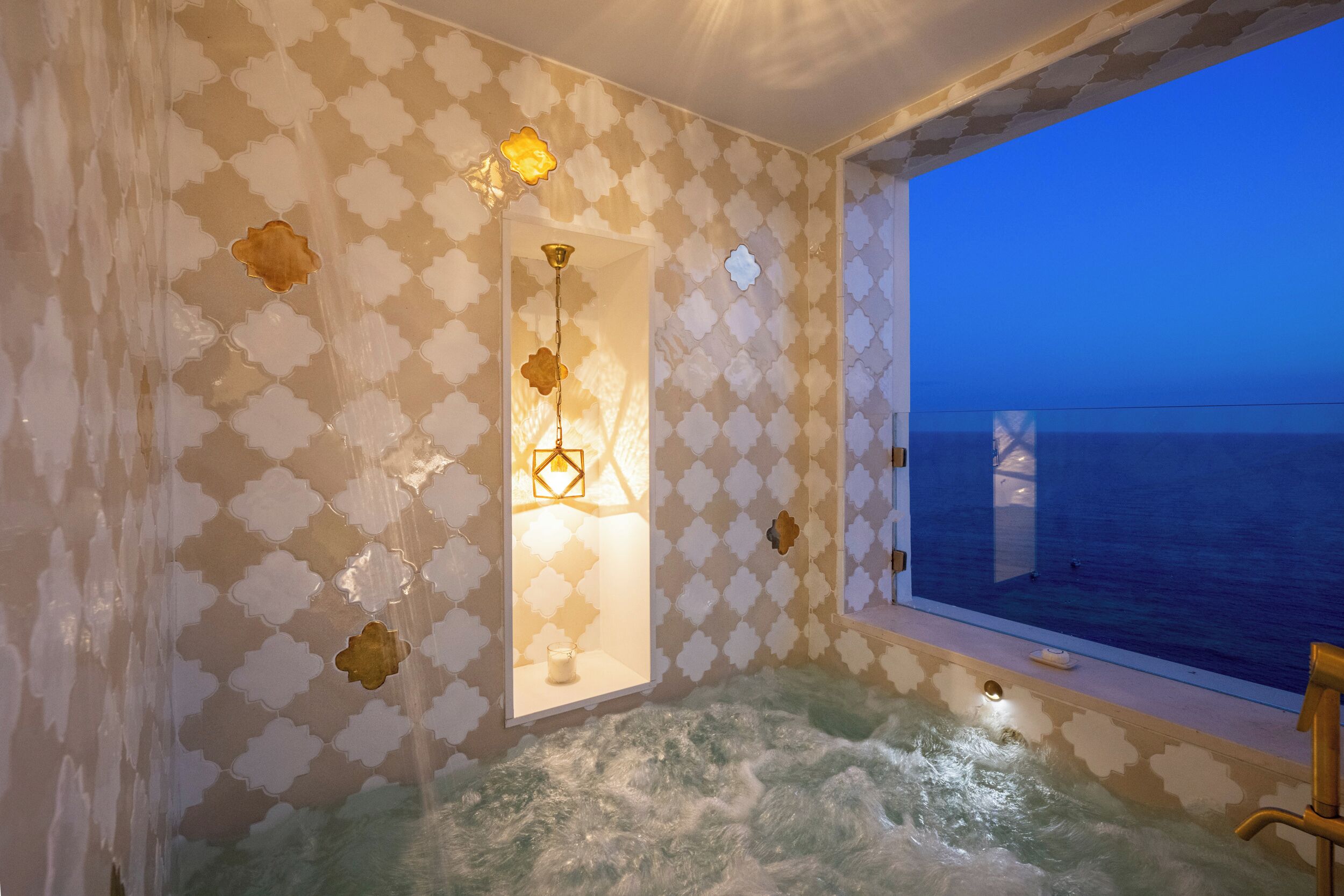 Une pièce dotée d’une grande fenêtre donnant sur la mer, d’une baignoire remplie d’eau et de murs aux motifs décoratifs.